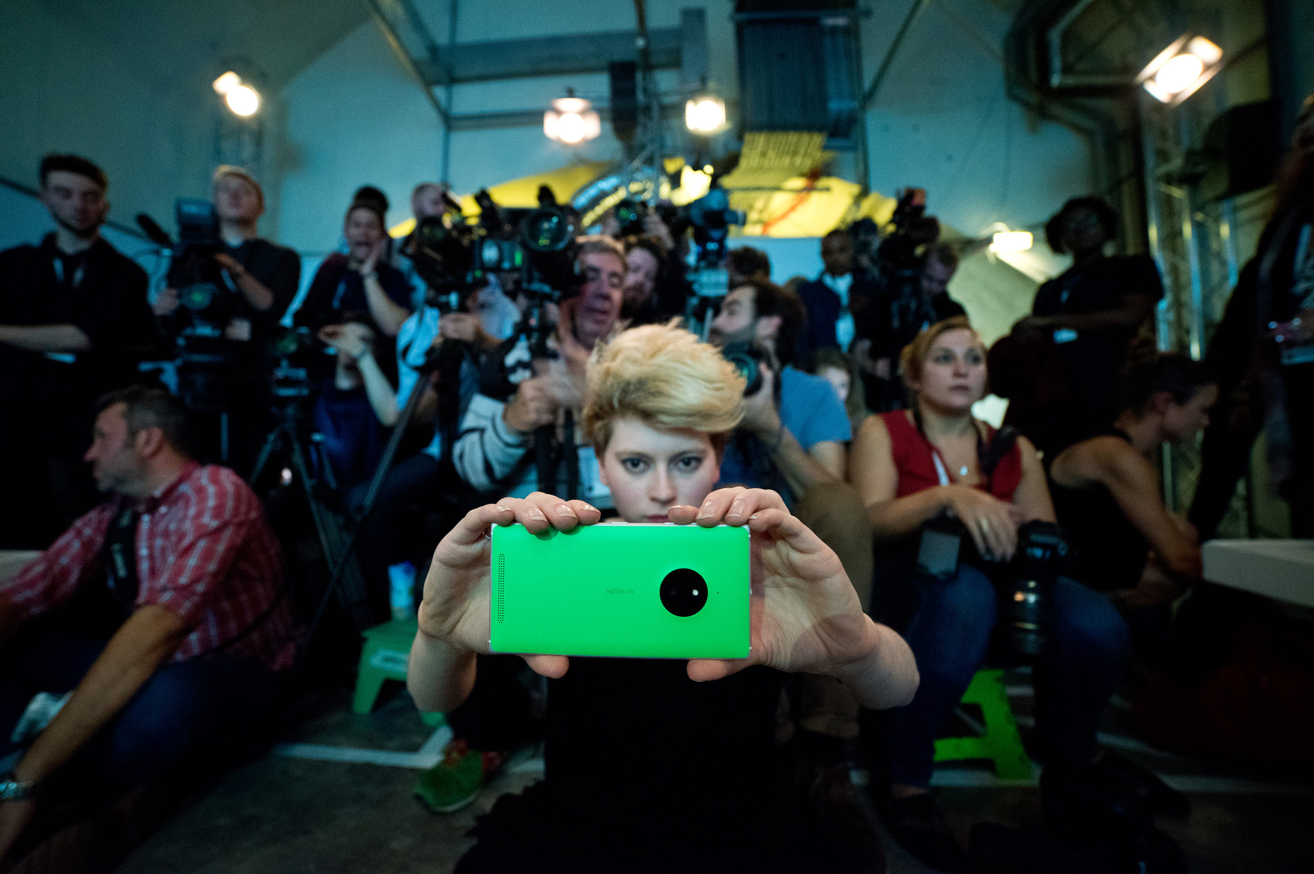 Girl holding smart phone in front of crowd at a fashion show, Fashion Innovation Agency